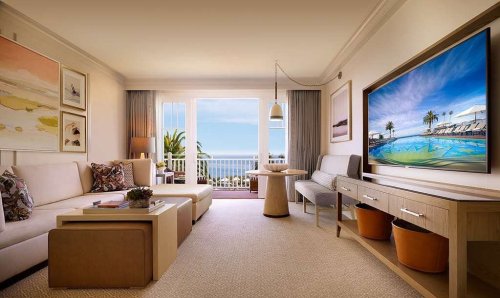 Bright, modern hotel room with a view of the ocean, featuring a sofa, artwork, and a large TV.