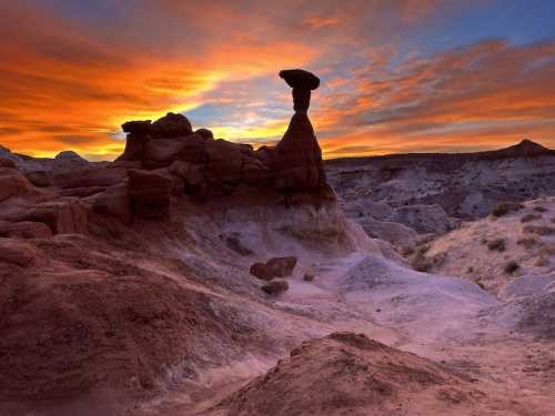 A striking rock formation stands against a vibrant sunset sky in a desert landscape.