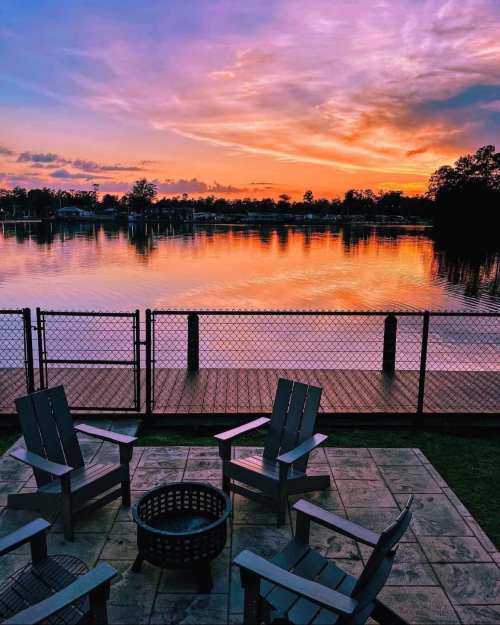 A serene lakeside view at sunset, featuring chairs around a fire pit and vibrant colors reflecting on the water.