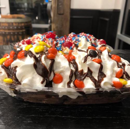 A close-up of a dessert platter featuring whipped cream, chocolate drizzle, and colorful toppings like candy and sprinkles.