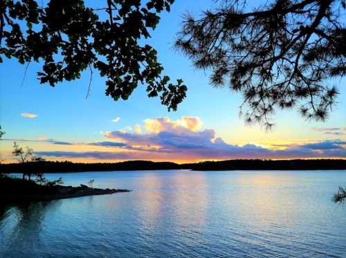 A serene lake at sunset, with colorful clouds reflecting on the water and trees framing the scene.