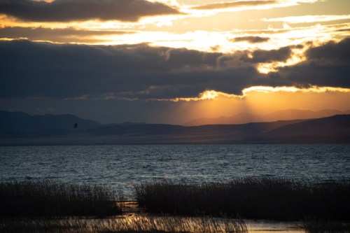 A serene sunset over a lake, with clouds and mountains silhouetted against the colorful sky.