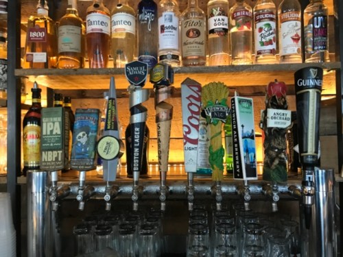 A bar display featuring various beer taps and bottles on shelves, showcasing a variety of brands and styles.