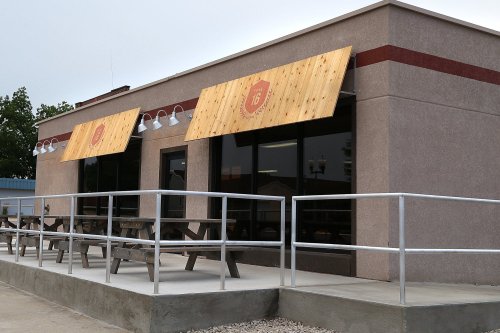 Exterior of a restaurant with wooden awnings, large windows, and outdoor seating area.