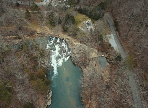 Aerial view of a winding river with rapids, surrounded by bare trees and a gravel road nearby.
