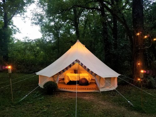 A cozy tent set in a wooded area, illuminated from within, with decorative lights and a welcoming entrance.