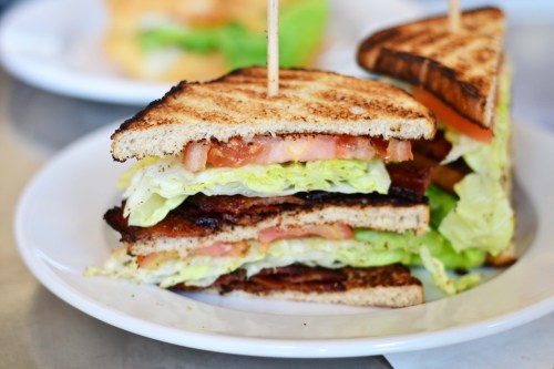 A stacked sandwich with toasted bread, layers of lettuce, tomato, and bacon, served on a white plate.