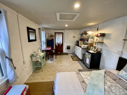 Cozy interior of a small room with a bed, dining table, kitchenette, and natural light from windows.