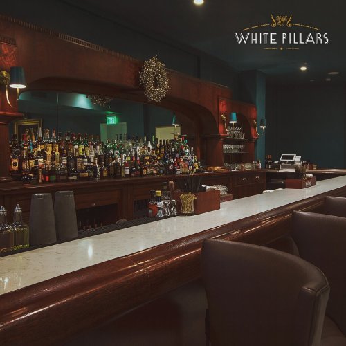 A stylish bar with a marble countertop, shelves lined with various liquor bottles, and elegant lighting.