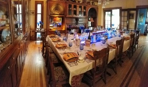 A beautifully set dining table with blue glassware, surrounded by wooden chairs in an elegant room.