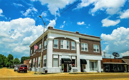 Historic brick building with an awning, American flag, and blue sky with clouds in a small town setting.