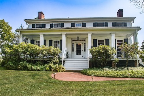 A charming white house with a porch, surrounded by greenery and a well-maintained lawn under a clear blue sky.