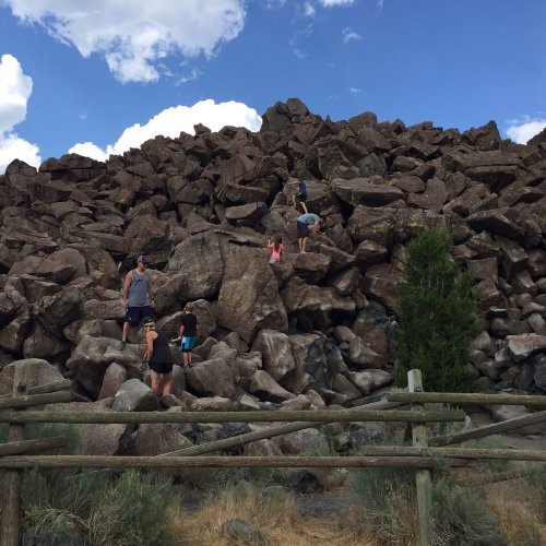 A group of people climbing a large rock formation under a blue sky with clouds.