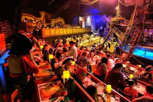 A lively dining scene with guests in pirate costumes, enjoying a themed show in a ship-like setting.