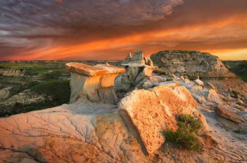 A stunning landscape featuring rocky formations under a vibrant sunset sky with dramatic clouds.