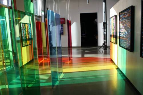 A colorful art installation with transparent panels creating vibrant reflections and shadows in a gallery space.