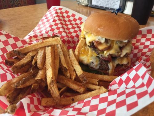 A juicy cheeseburger with multiple patties and melted cheese, served with a side of crispy French fries in a red-checkered basket.