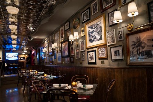 Cozy restaurant interior with wooden tables, candlelight, and walls adorned with framed artwork and photographs.