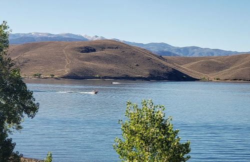 A serene lake surrounded by hills, with a boat gliding across the water under a clear blue sky.