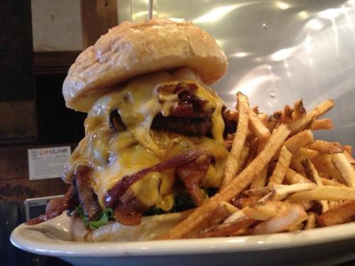 A towering cheeseburger with bacon and lettuce, served with a side of crispy French fries.