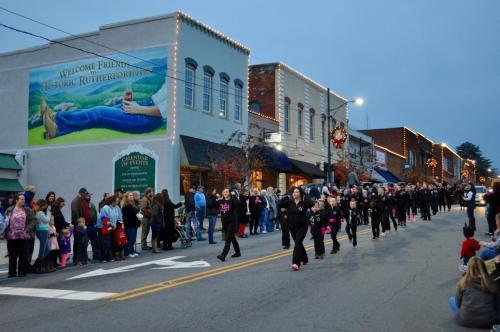 A parade with participants in black outfits marching down a street lined with spectators and festive decorations.