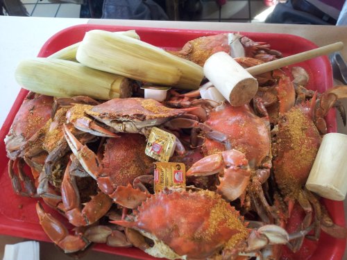 A red tray filled with seasoned crabs, corn on the cob, and a small mallet for cracking shells.