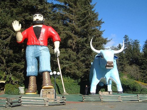 Giant statues of Paul Bunyan and a blue ox, surrounded by trees and a clear blue sky.