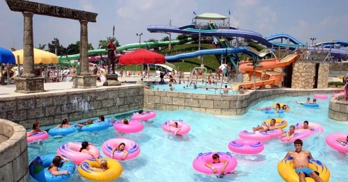 A busy water park scene with colorful inner tubes floating in a lazy river, surrounded by water slides and sunbathers.