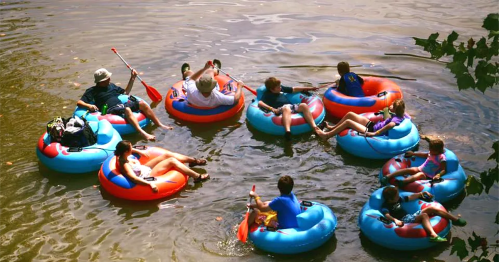 A group of people relaxing on colorful inner tubes in a river, some paddling and others lounging.