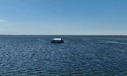 A small boat with a roof floats on calm water under a clear blue sky.