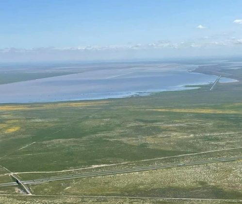 Aerial view of a vast landscape with green fields, a body of water, and a clear blue sky.
