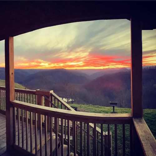 A scenic view of a sunset over rolling hills, framed by a wooden porch railing.