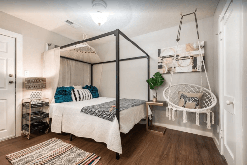 Cozy bedroom featuring a four-poster bed, hanging chair, and decorative rugs in a modern, minimalist style.