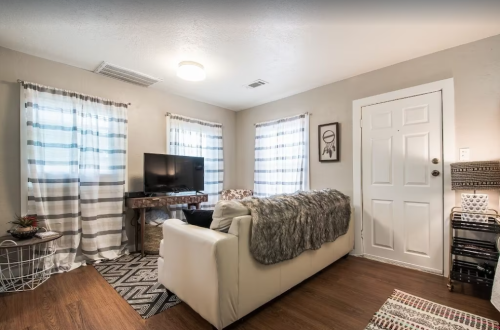 Cozy living room with a white couch, TV, striped curtains, and decorative accents on wooden flooring.