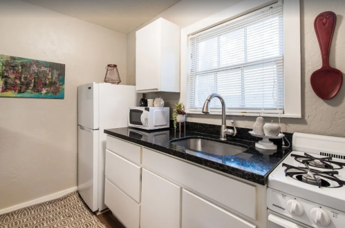 A modern kitchen featuring white cabinets, a black countertop, a sink, and appliances including a refrigerator and stove.