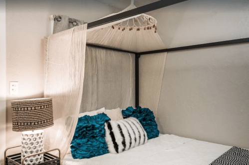 A cozy bedroom with a four-poster bed draped in sheer fabric and decorative teal and black pillows.