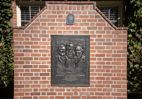Bronze plaque depicting four figures, mounted on a brick wall, with a seal above it.
