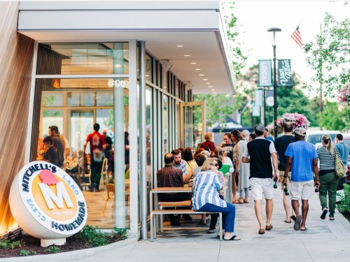 A bustling outdoor scene at Mitchell's Ice Cream, with people enjoying treats and walking along the sidewalk.