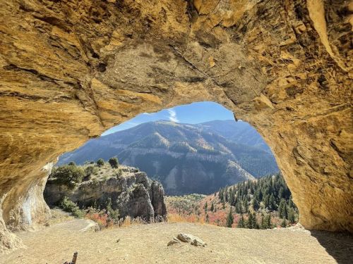 A scenic view from inside a cave, showcasing mountains and colorful autumn foliage in the background.