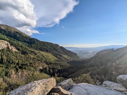 A scenic view of a valley surrounded by mountains, with lush greenery and a clear blue sky.