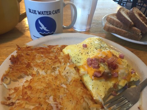 A plate with an omelet, hash browns, and toast, alongside a coffee mug and a glass of water.