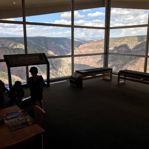 A spacious room with large windows showcasing a scenic mountain view, featuring two children exploring an exhibit.