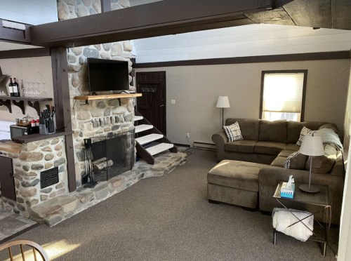 Cozy living room with a stone fireplace, TV, sofa, and a small dining area, featuring warm lighting and neutral decor.
