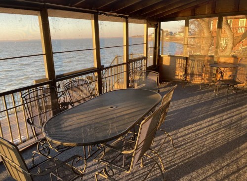 A screened porch with a table and chairs overlooking a calm lake at sunset.
