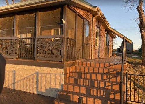 A wooden deck leads up to a house with a screened porch and decorative railing, illuminated by warm evening light.