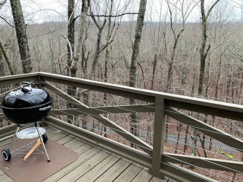 A black grill on a wooden deck overlooking a forest of bare trees in winter.