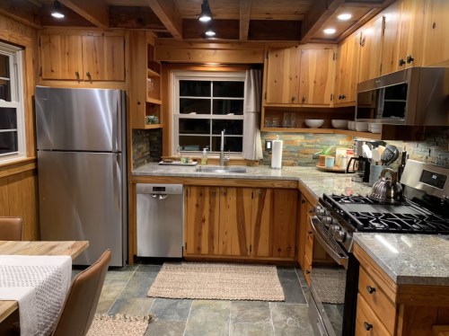 Cozy wooden kitchen with stainless steel appliances, stone accents, and a dining area featuring a table and chairs.