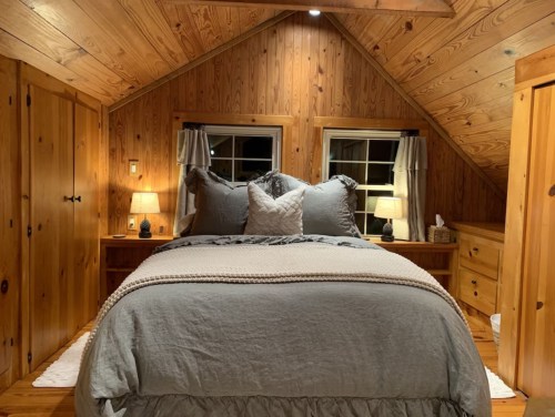 Cozy bedroom with wooden walls, a large bed, two lamps, and windows, creating a warm, inviting atmosphere.