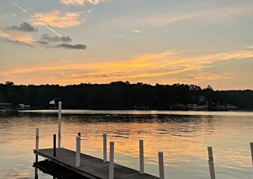 A serene lake at sunset, with a wooden dock and colorful sky reflecting on the water.
