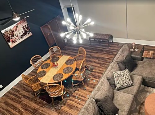 A cozy dining area with a wooden table, chairs, and a modern chandelier, adjacent to a comfortable living space.